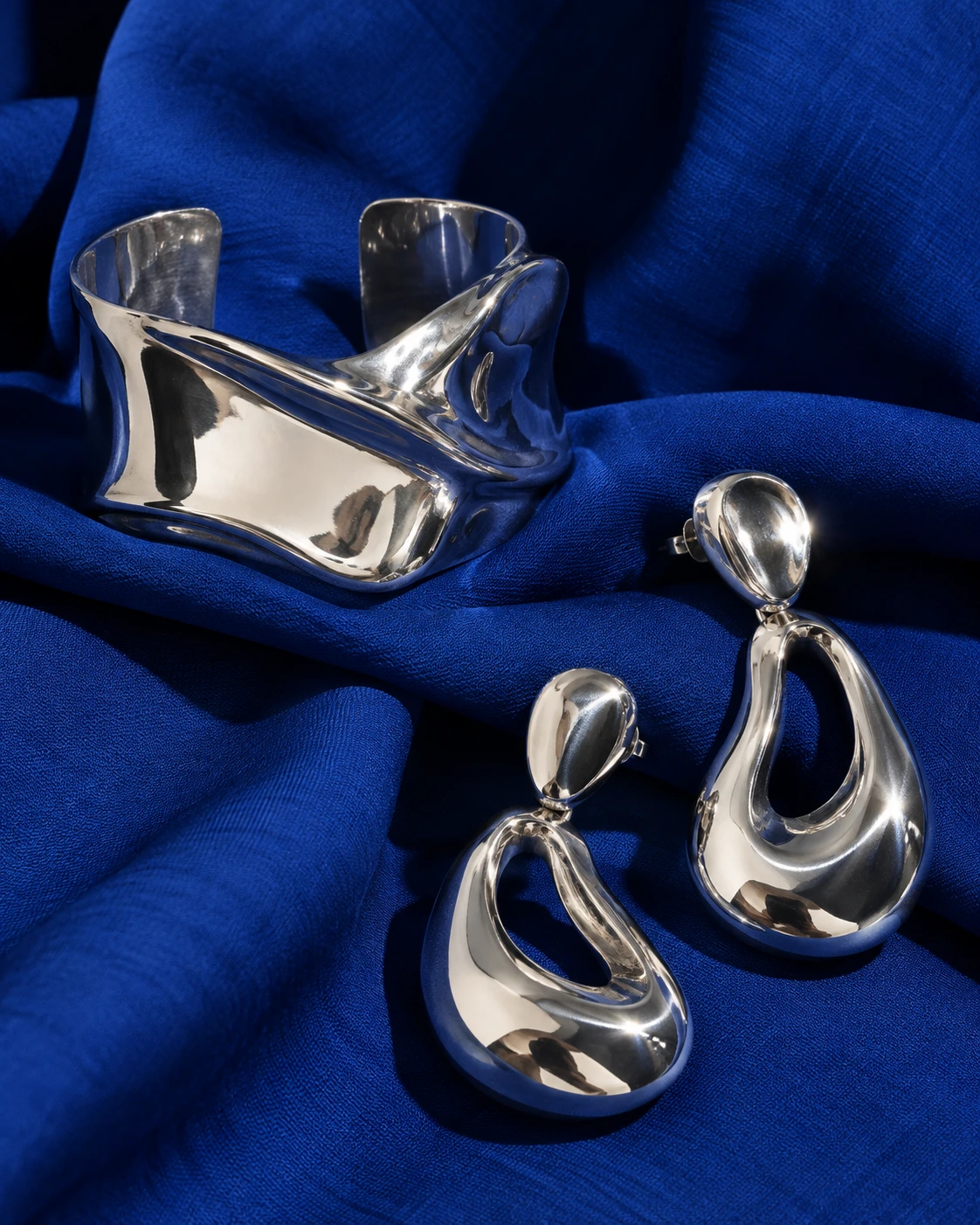 AI editorial concept: sculptural silver cuff and earrings on cobalt fabric